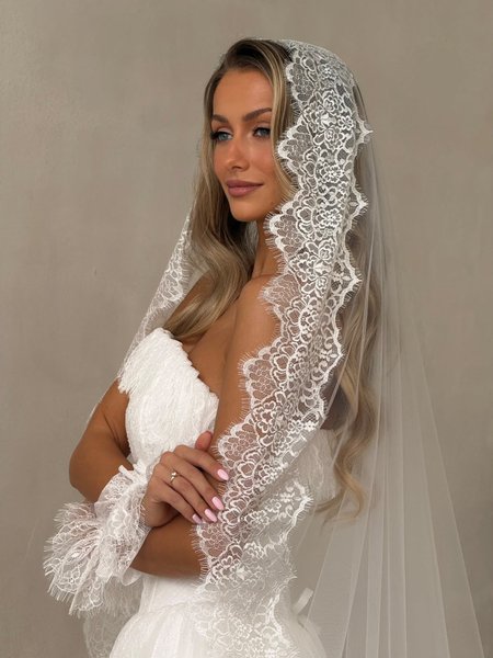 A cathedral-style wedding veil in a light ecru shade, adorned with delicate French lace